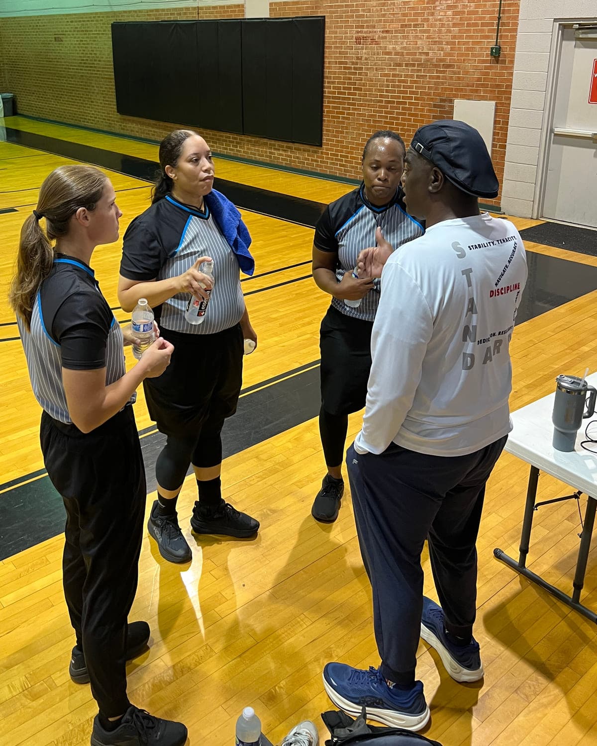 A clinician coaching three basketball officials courtside between games.